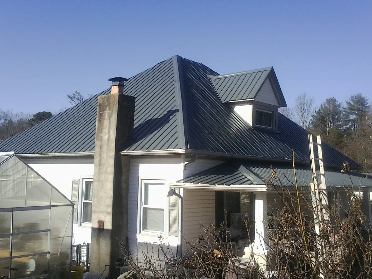 Dark blue standing seam metal roof on a white farmhouse with dormer — Slate & Tile Roof Repair by Roofing Brothers in Morriston
