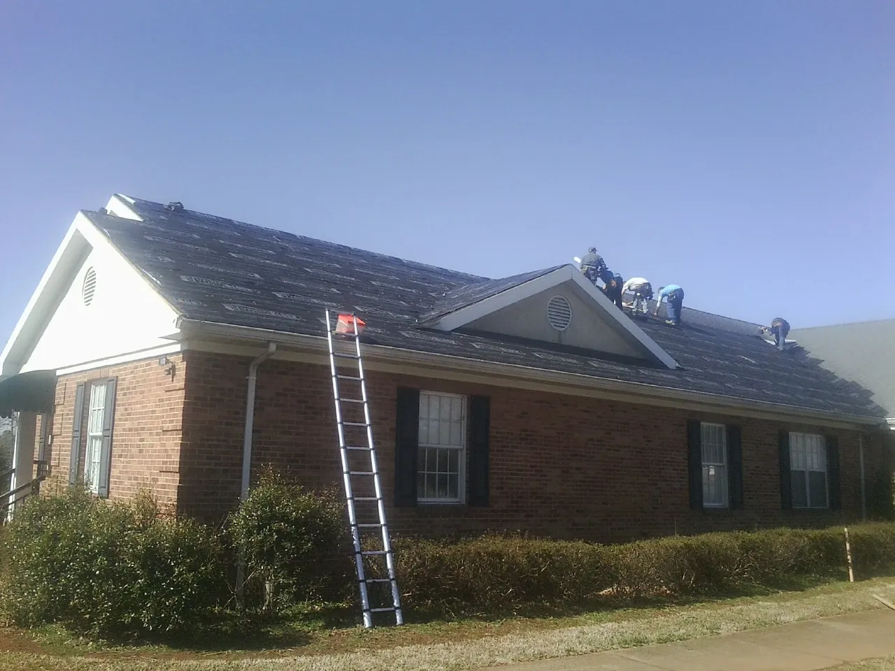 Crew tearing shingles off a brick ranch roof with a ladder set — Emergency Roof Repair work by our crew in Morriston