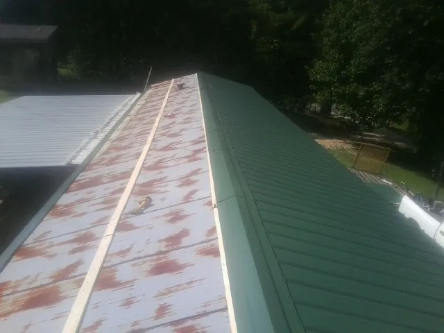 Old rusted panels beside newly installed green metal roofing — Wind Damage Roof Repair by Roofing Brothers in Morriston