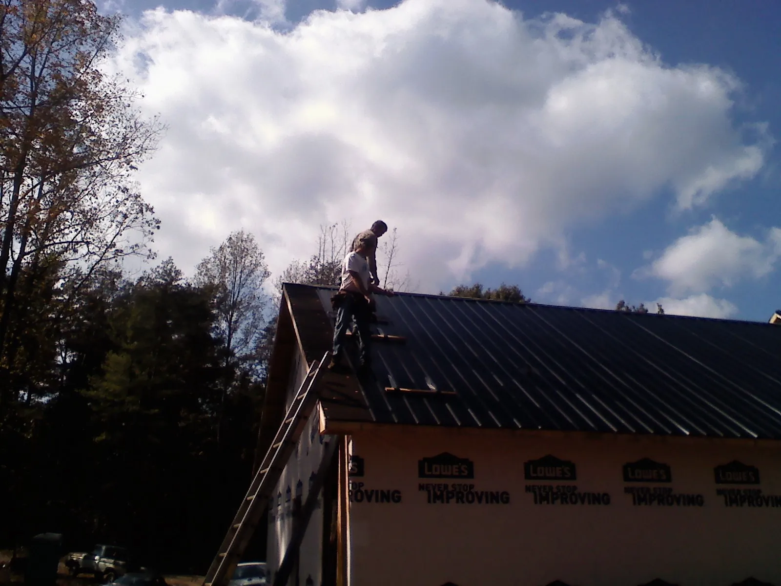 Roofer fastening dark metal panels high against a cloudy sky, from a Roof Inspection job in Morriston