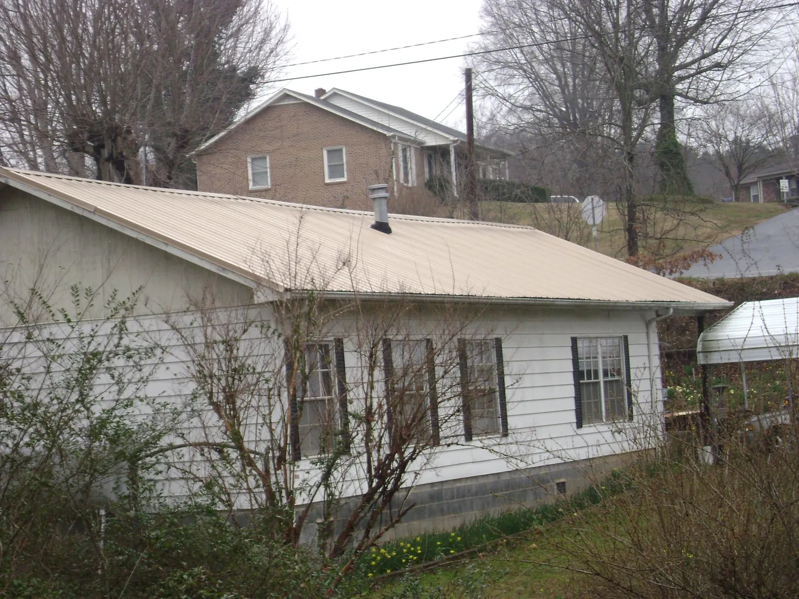 Tan metal roof on a white sided house set into a hillside — Commercial Roofing by Roofing Brothers in Morriston